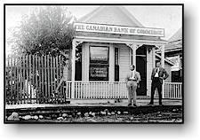 Exterior of historical CIBC in Nakusp. There are two men standing in front of the bank posing for the photo.
