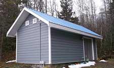 Exterior of micro generation station. It looks like a small, grey shed in the middle of the woods.